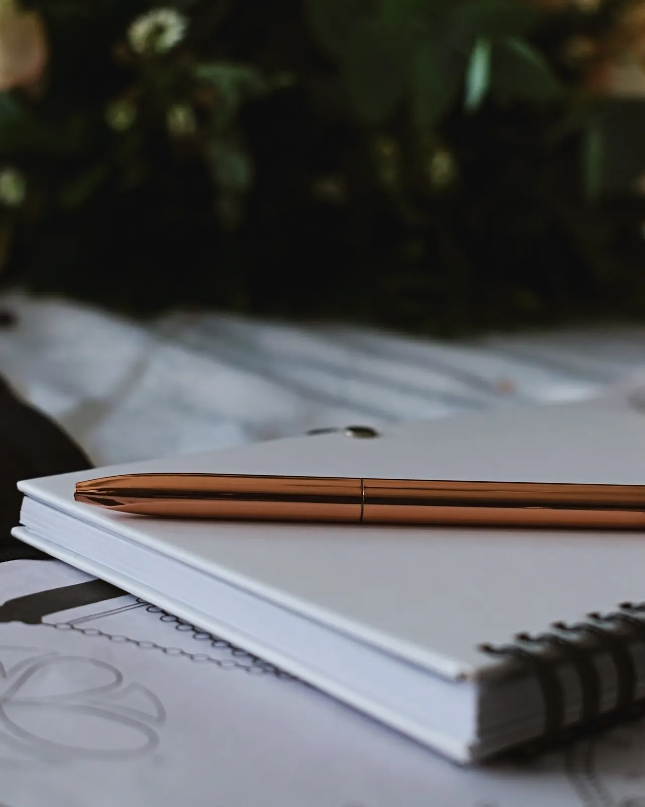 A gold pen resting on a closed notebook beside a stack of papers