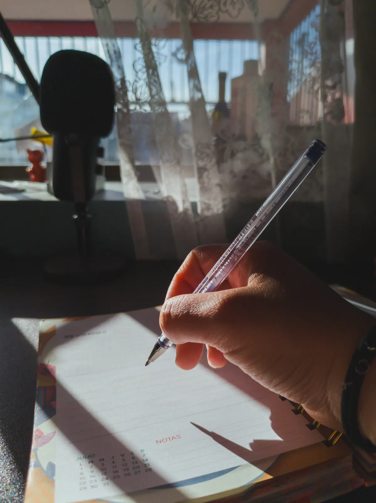 A hand writing in a lined notebook beside a window